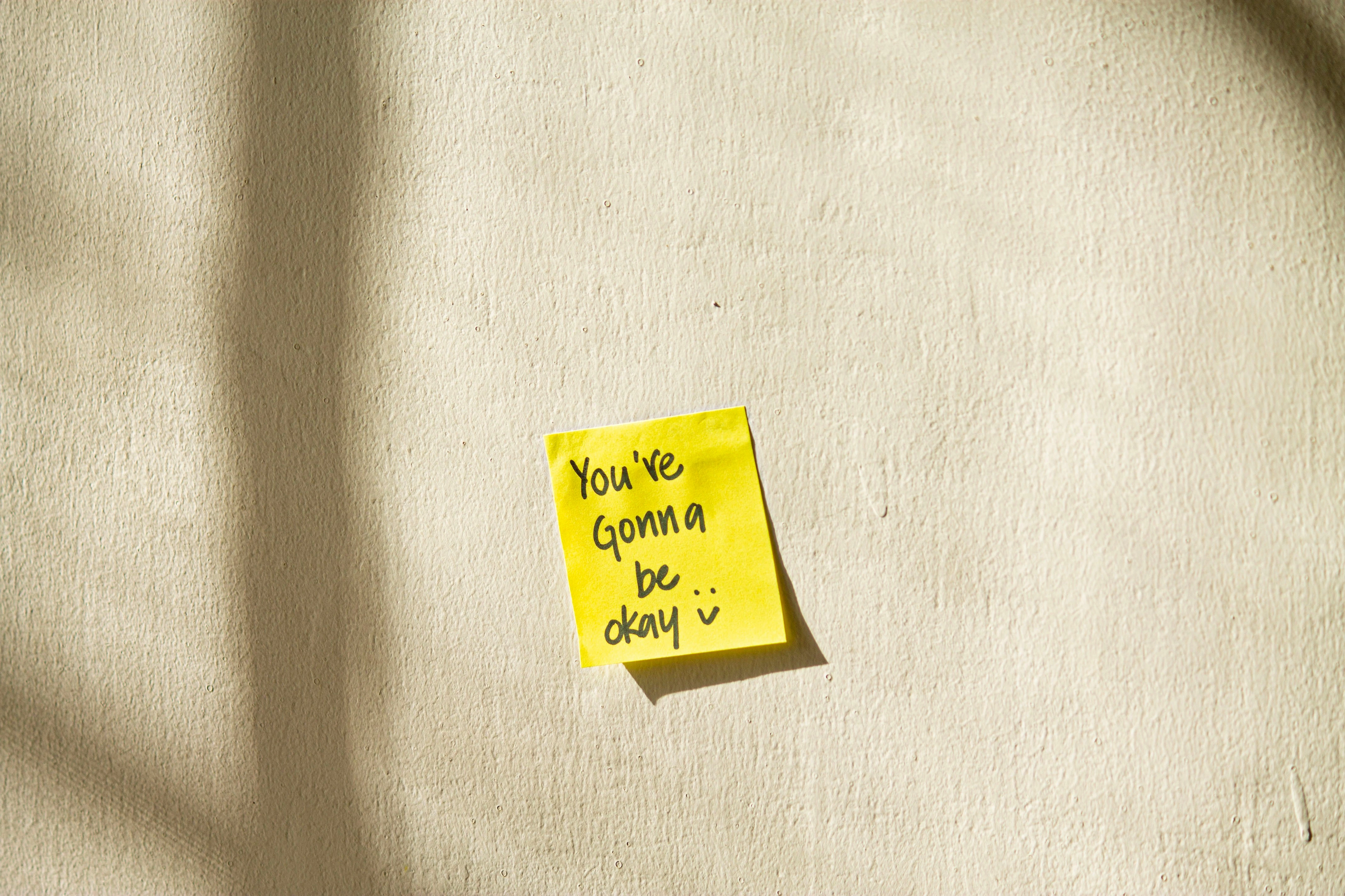 Image of a sticky note pasted on the wall with handwritten message 'you're going to be ok :-)' 